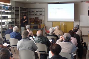 画面左で講師が解説し、画面手前で聴講者が話に耳を傾ける様子が映る