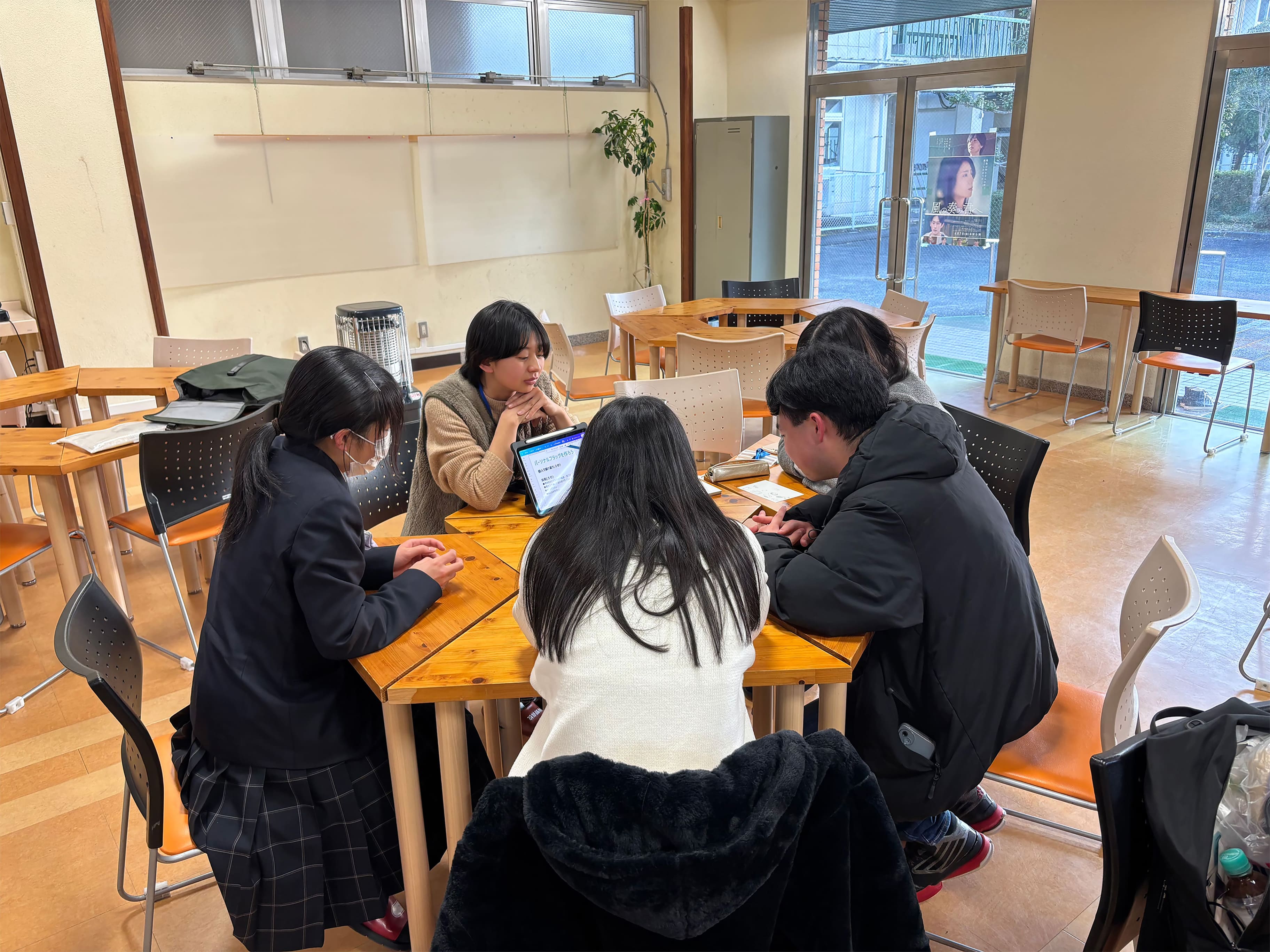 パソコンを5人の学生で囲み話し合っている様子