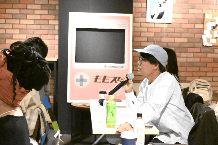 マイクを持って机に座りながら話している参加者の写真