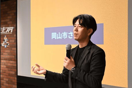 スクリーンの前でしゃべっている男性の写真